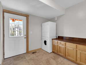 Laundry room with stacked washer and dryer, cabinets, and light tile floors