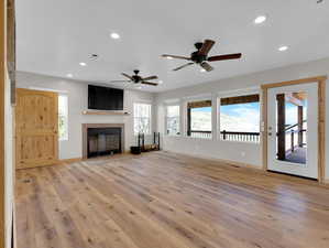 Unfurnished living room with ceiling fan, a tiled fireplace, and light hardwood / wood-style flooring