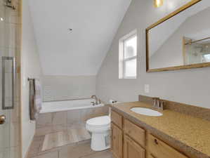 Bathroom featuring tile flooring, lofted ceiling, tiled tub, vanity with extensive cabinet space, and toilet