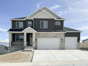 Craftsman house with driveway, stone siding, covered porch, fence, and board and batten siding