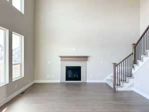 Unfurnished living room featuring baseboards, a high ceiling, stairway, and light wood-style floors