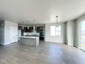 Kitchen with light countertops, appliances with stainless steel finishes, a sink, light wood-type flooring, and wall chimney exhaust hood