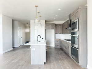 Kitchen featuring a sink, light countertops, light wood-type flooring, backsplash, and wall chimney exhaust hood