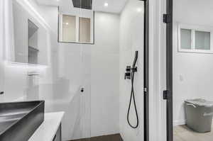 Bathroom with tiled shower, vanity, and tile floors