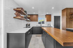 Kitchen featuring tasteful backsplash, butcher block countertops, black electric cooktop, light tile flooring, and sink