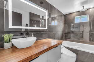 Bathroom featuring tile walls, a textured ceiling, vanity, and bidet toilet