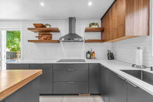 Kitchen featuring backsplash, black electric stovetop, wall chimney exhaust hood, gray cabinets, and light tile floors