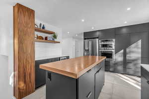 Kitchen featuring light tile flooring, a kitchen island, stainless steel appliances, backsplash, and butcher block countertops