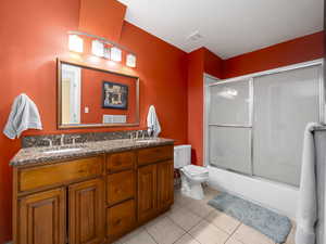 Full bathroom featuring dual vanity, shower / bath combination with glass door, tile floors, and toilet