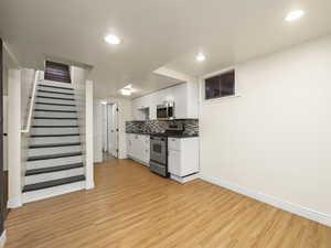 Kitchen featuring stainless steel appliances, light hardwood / wood-style floors, white cabinets, and backsplash