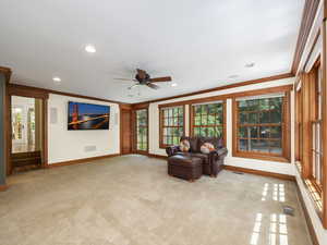 Living room featuring ceiling fan, carpet floors,  crown molding, and lots of windows