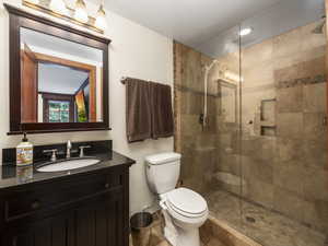 Bathroom off of the living room,  featuring a shower with shower door, vanity, toilet, and tile floors