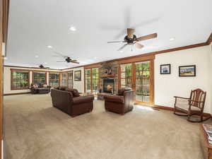 Living room with light carpet, ceiling fan, a fireplace,  crown molding, and lots of windows