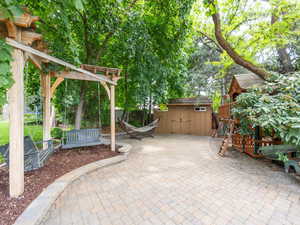 Backyard terrace featuring pergola swings, a high end playhouse, and a storage shed