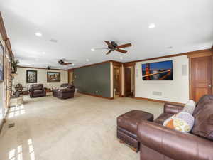 Living room with ceiling fan, carpet floors, crown molding, and lots of windows