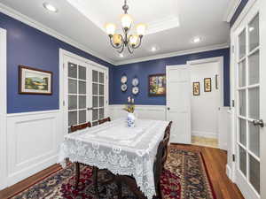 Dining room with a chandelier, a raised ceiling, crown molding, hardwood / wood-style floors, and French doors