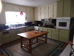 Kitchen featuring dark wood-type flooring, oven, sink, tasteful backsplash, and dishwasher