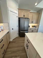 Kitchen with decorative backsplash, light brown cabinetry, stainless steel fridge, and wood-type flooring