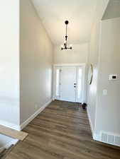 Foyer entrance with high vaulted ceiling, an inviting chandelier, and dark hardwood / wood-style floors