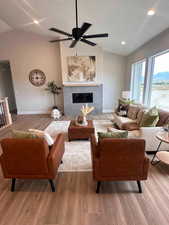 Living room with a fireplace, a textured ceiling, hardwood / wood-style flooring, ceiling fan, and vaulted ceiling