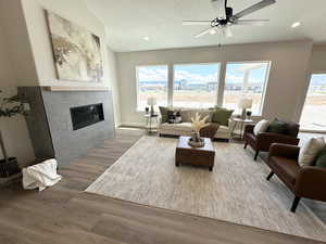 Living room featuring a textured ceiling, ceiling fan, light wood-type flooring, and a tile fireplace