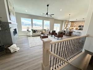 Living room with a fireplace, light hardwood / wood-style floors, ceiling fan with notable chandelier, and a textured ceiling