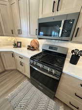 Kitchen with light wood-type flooring, appliances with stainless steel finishes, backsplash, and light brown cabinetry