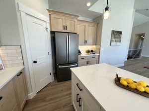 Kitchen with hardwood / wood-style floors, decorative backsplash, stainless steel refrigerator, light brown cabinets, and pendant lighting