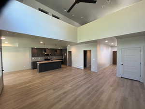 Unfurnished living room featuring ceiling fan, light hardwood / wood-style flooring, a towering ceiling, and sink