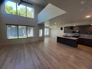 Kitchen with stainless steel appliances, hanging light fixtures, an island with sink, wood-type flooring, and sink