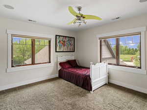 Carpeted bedroom with ceiling fan and multiple windows