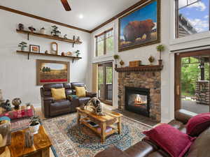 Living room with a towering ceiling, ceiling fan, a fireplace, and crown molding