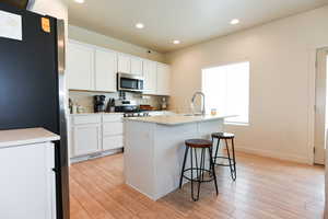 Kitchen featuring an island with sink, white cabinets, light hardwood / wood-style flooring, and stainless steel appliances