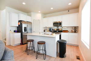 Kitchen with a wealth of natural light, a center island with sink, appliances with stainless steel finishes, and white cabinetry