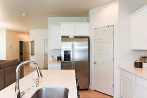 Kitchen with sink, white cabinetry, stainless steel fridge, and light hardwood / wood-style floors