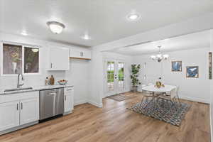 Kitchen featuring white cabinetry, light stone countertops, light wood-type flooring, sink, and dishwasher