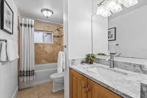 Full bathroom with tile flooring, vanity, toilet, and shower / tub combo with curtain