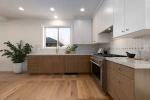 Kitchen featuring backsplash, white cabinets, high end range, and light wood-type flooring