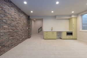 Kitchen with green cabinetry, light carpet, sink, and brick wall