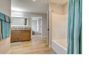 Bathroom with shower / bathtub combination with curtain, wood-type flooring, and vanity