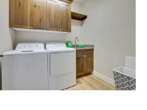 Washroom with washing machine and dryer, sink, light hardwood / wood-style floors, and cabinets