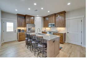 Kitchen featuring sink, a kitchen island with sink, light wood-type flooring, and stainless steel appliances