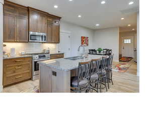 Kitchen featuring light hardwood / wood-style floors, a center island with sink, a kitchen bar, appliances with stainless steel finishes, and sink