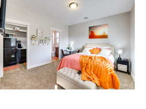 Carpeted bedroom featuring connected bathroom and black refrigerator