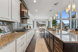 Kitchen with sink, dark wood-type flooring, pendant lighting, dark brown cabinets, and a center island with sink