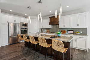 Kitchen with sink, dark wood-type flooring, built in appliances, an island with sink, and white cabinets