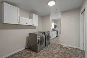 Washroom featuring cabinets, dark tile flooring, and washing machine and clothes dryer