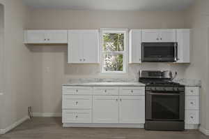 Kitchen featuring light stone countertops, stainless steel appliances, light hardwood / wood-style floors, and white cabinetry