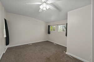 Carpeted spare room with ceiling fan and vaulted ceiling