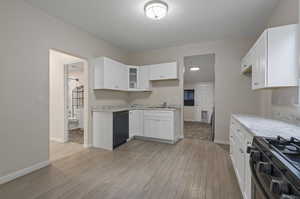 Kitchen featuring sink, light hardwood / wood-style floors, black dishwasher, white cabinets, and stainless steel gas range